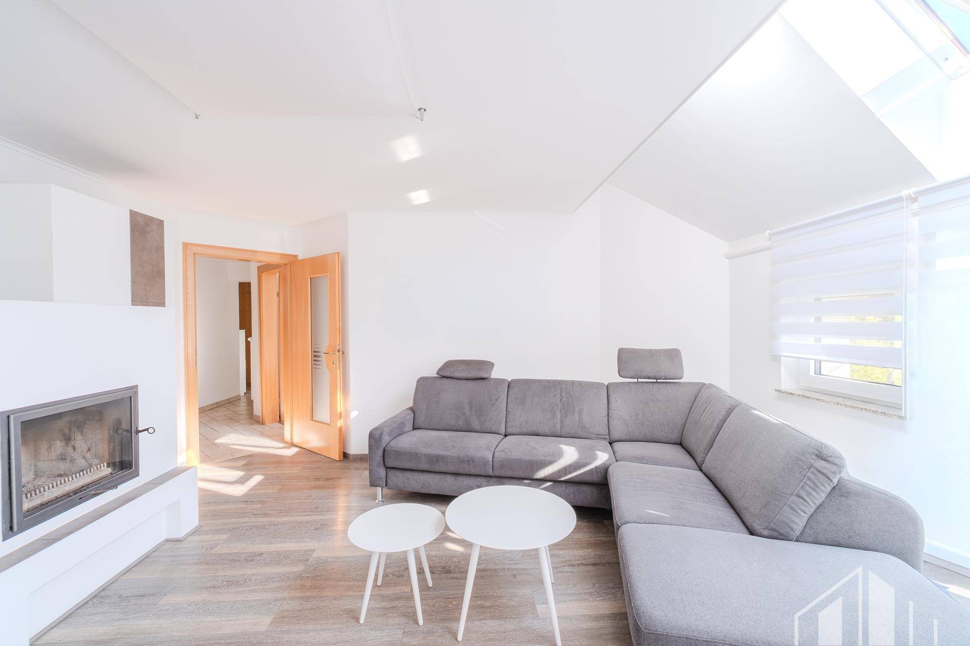 Helles Wohnzimmer mit modernem Sofa, Kamin und viel Tageslicht durch Dachfenster.