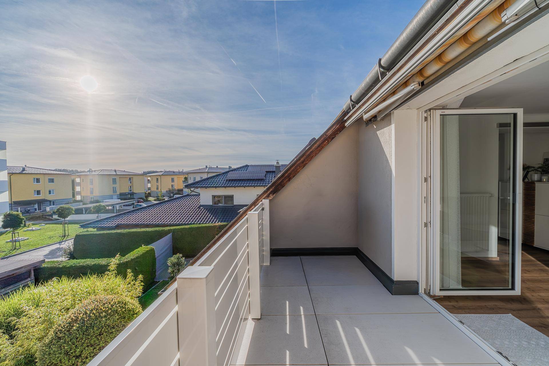 Sonniger Balkon mit Fliesenboden und weitem Blick über die Nachbarschaft und Dächer.