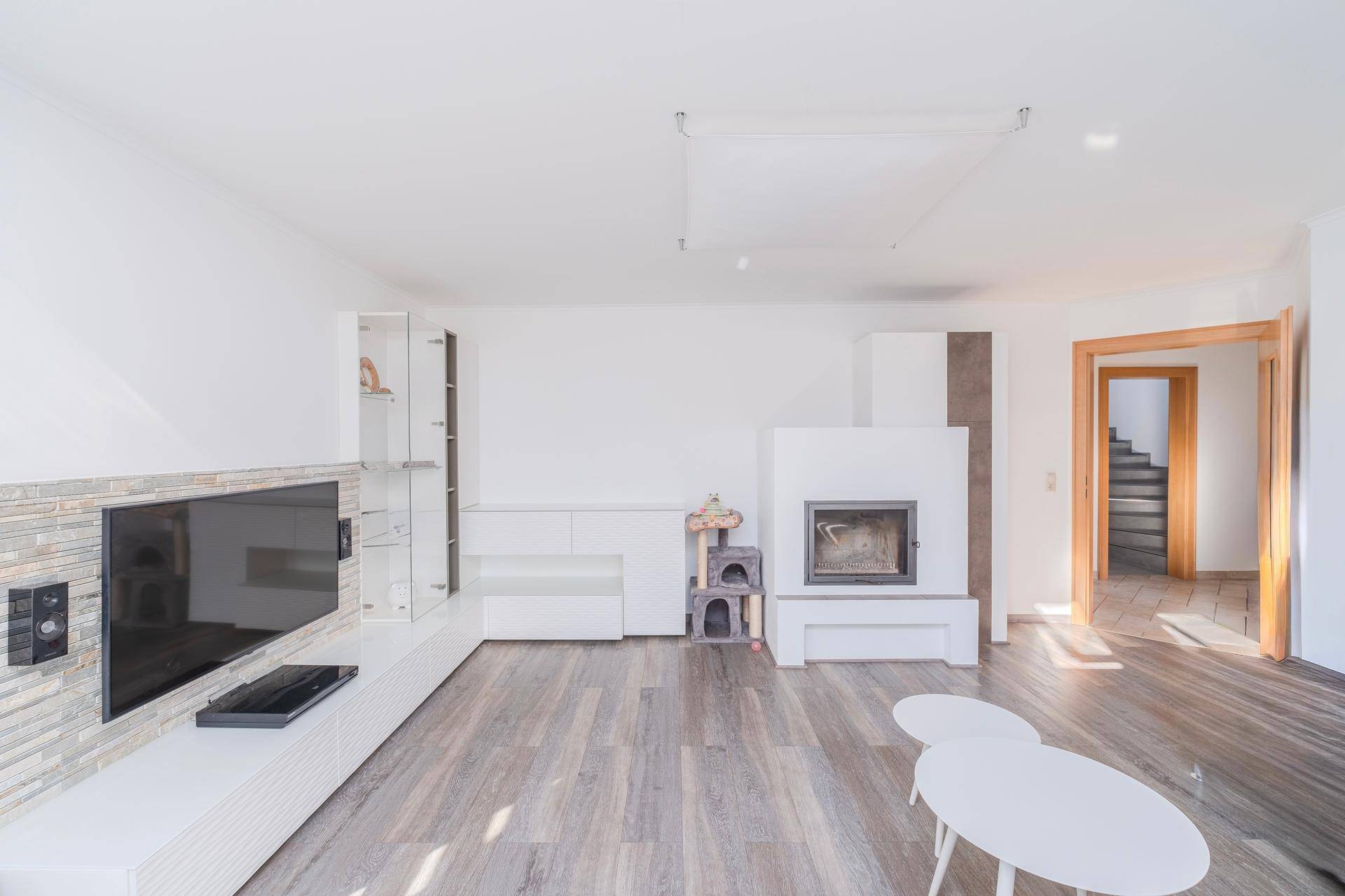 Helles Wohnzimmer mit modernem Kamin, integriertem TV-Bereich und Laminatboden, mit offenem Zugang zur Treppe.