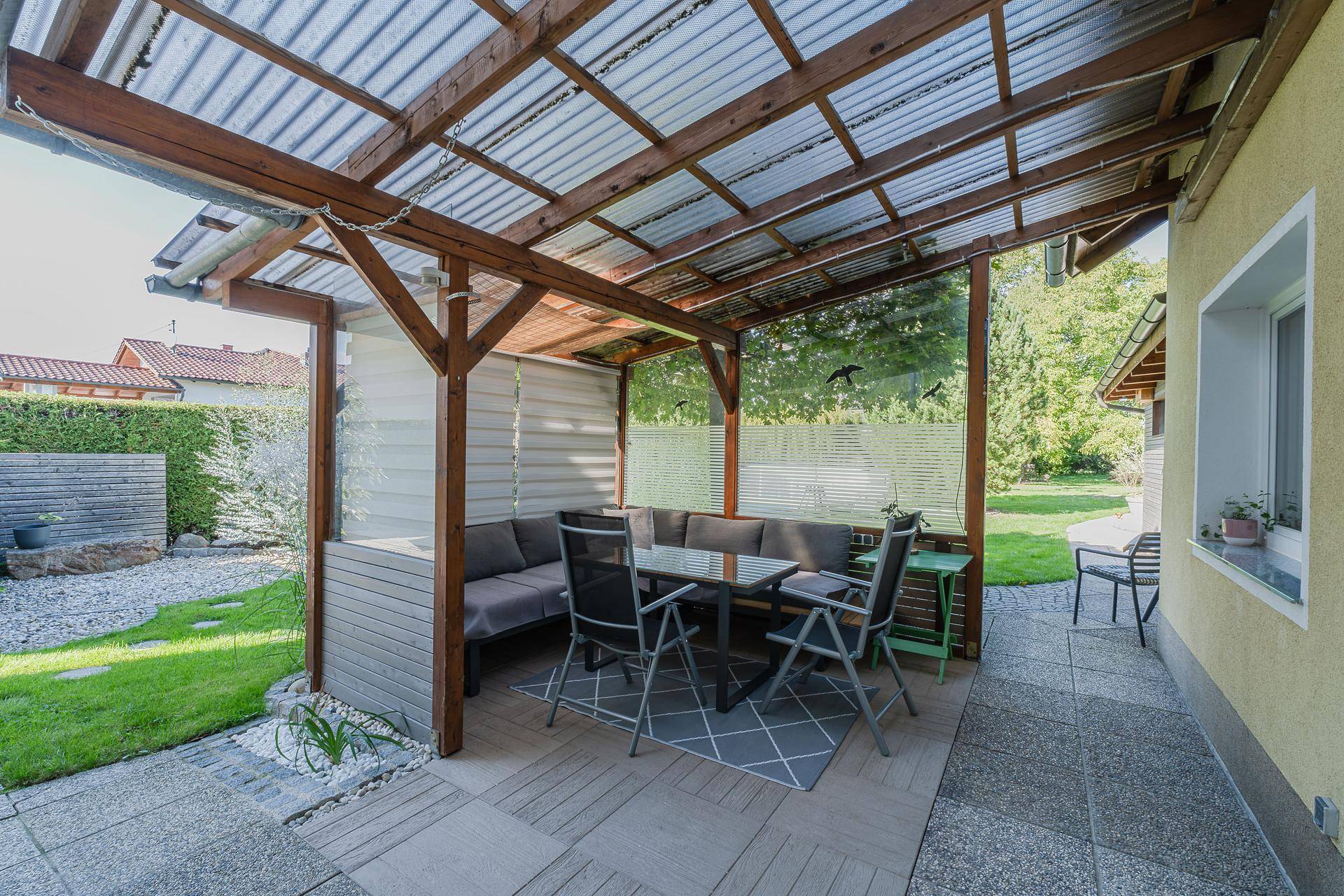 Überdachte Terrasse mit Sitzgelegenheiten, angrenzendem Rasen und einem Steingarten.