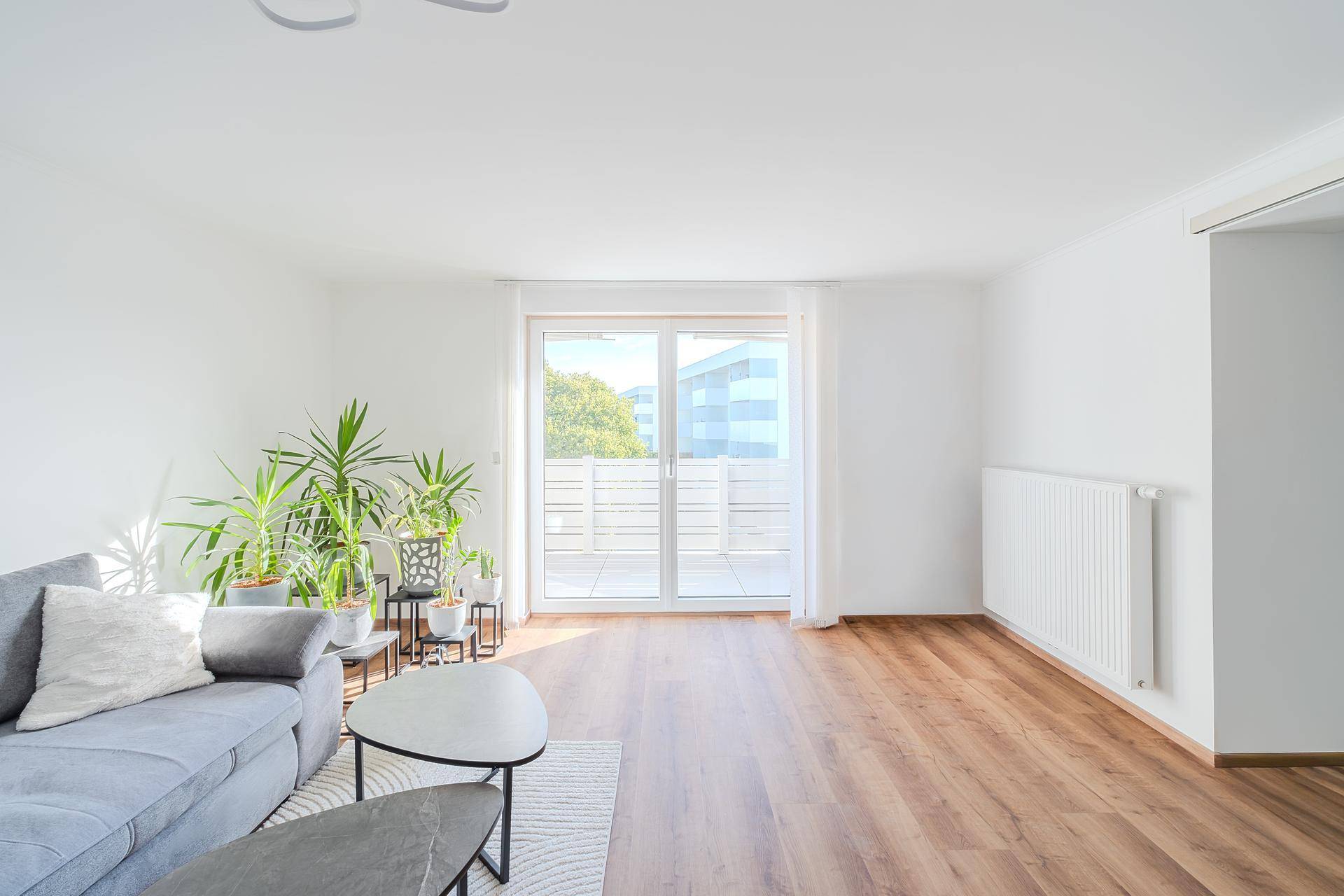 Helles Wohnzimmer mit Holzboden, Pflanzen und großen Schiebetüren zum Balkon.