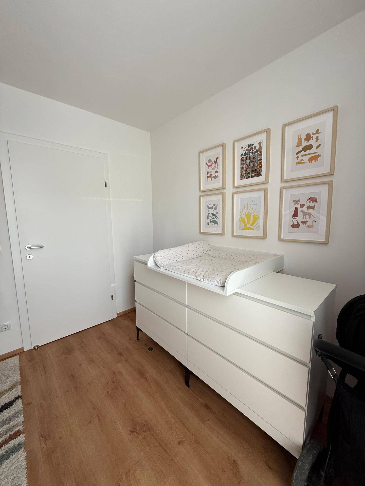 Kinderzimmer mit Wickelkommode und farbenfrohen Bildern an der Wand auf Laminatboden.