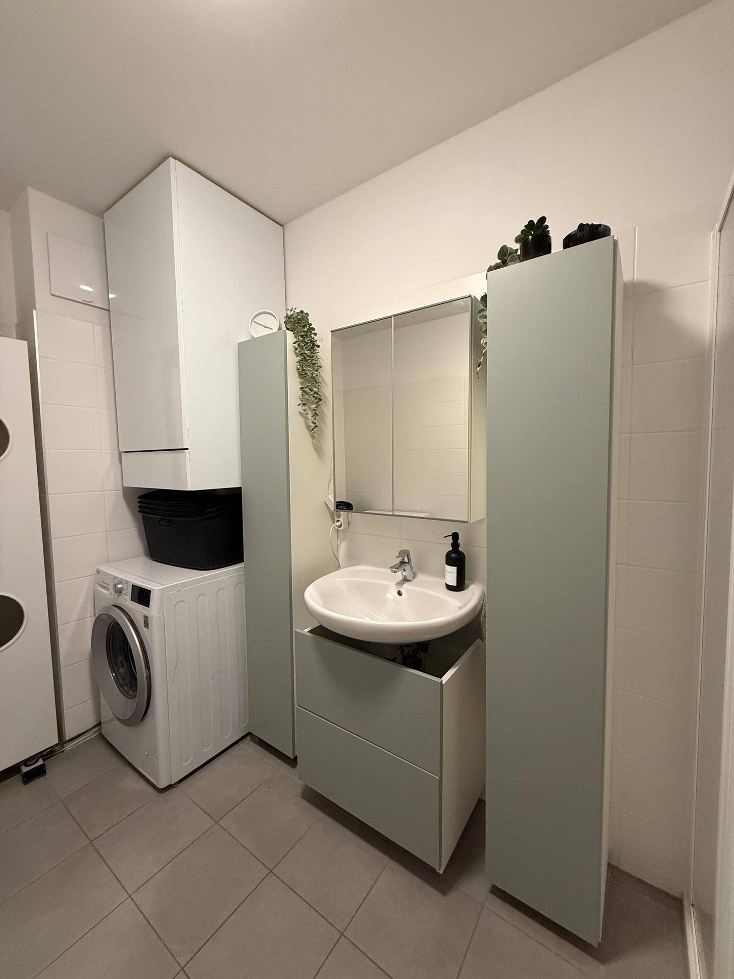 Badezimmer mit Waschbecken, Spiegelschrank, Waschmaschine und zusätzlichen Stauschränken.