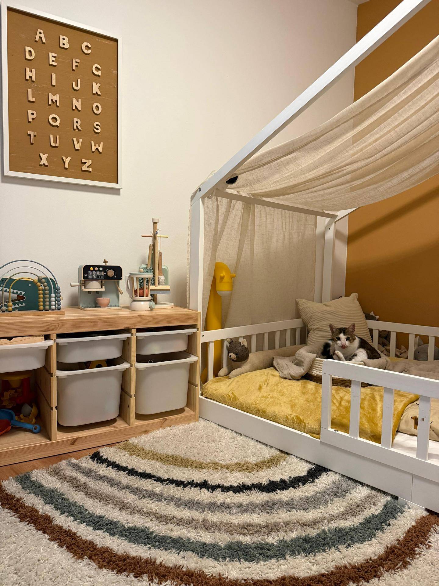Gemütliches Kinderzimmer mit Himmelbett, Spielbereich und einem Kätzchen auf dem Bett.