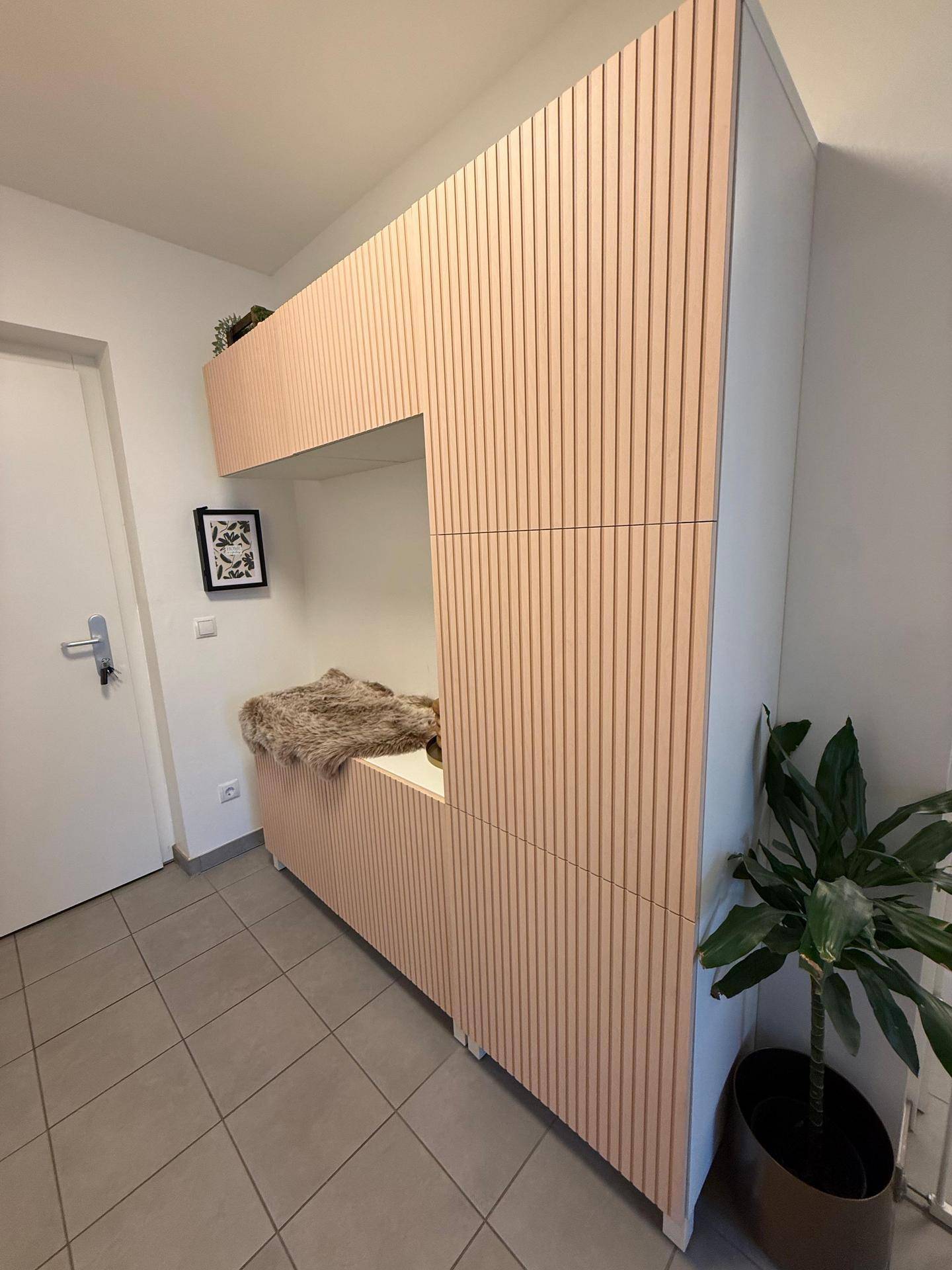 Moderner Eingangsbereich mit integriertem Stauraum, vertikalen Holzlamellen und Fliesenboden.