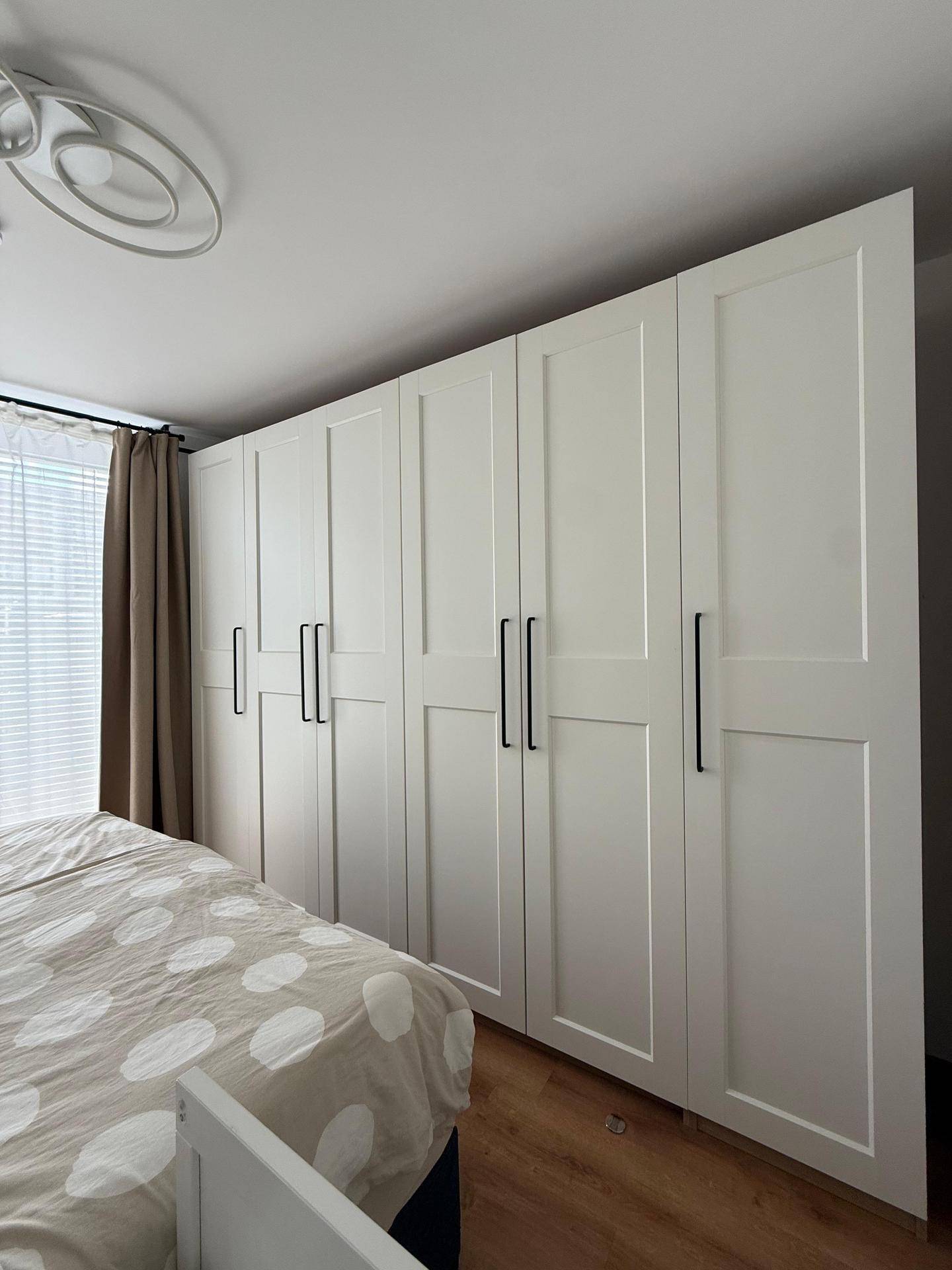 Schlafzimmer mit großem weißen Kleiderschrank und hellem Laminatboden.