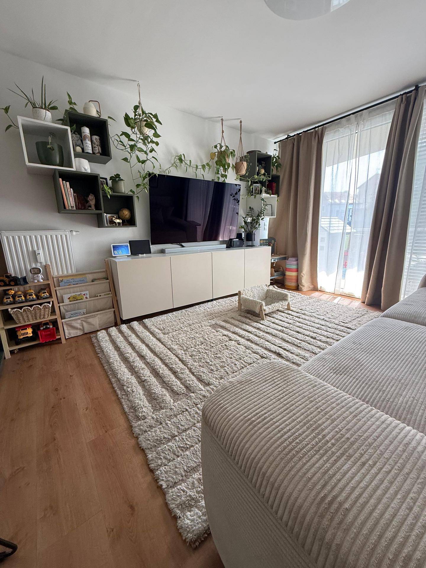 Gemütliches Wohnzimmer mit großem Fernseher, Mediamöbeln und dekorativen Pflanzen auf hellem Laminatboden.