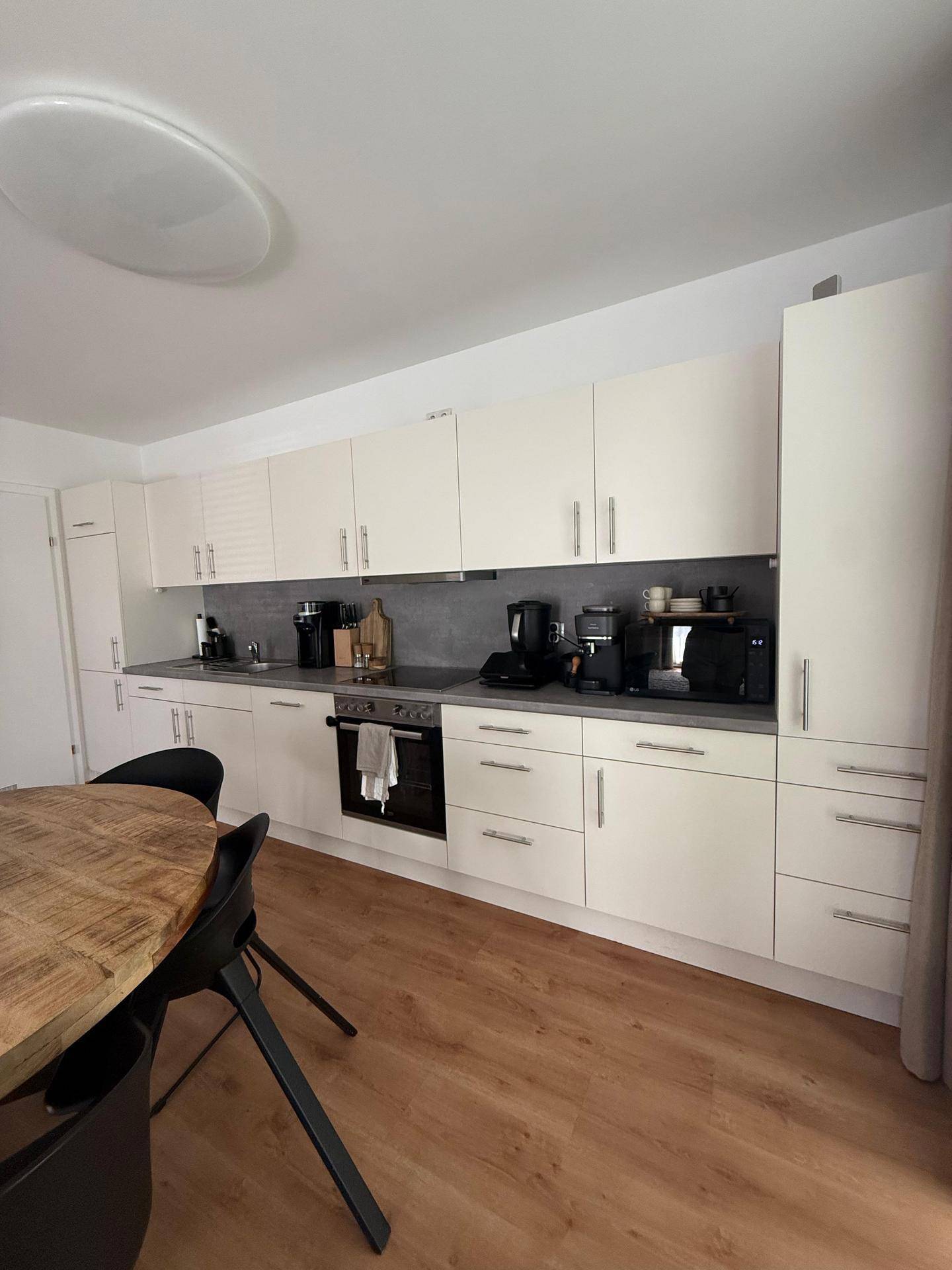 Moderne Einbauküche mit weißen Schränken, grauer Arbeitsplatte und Essbereich im Vordergrund.