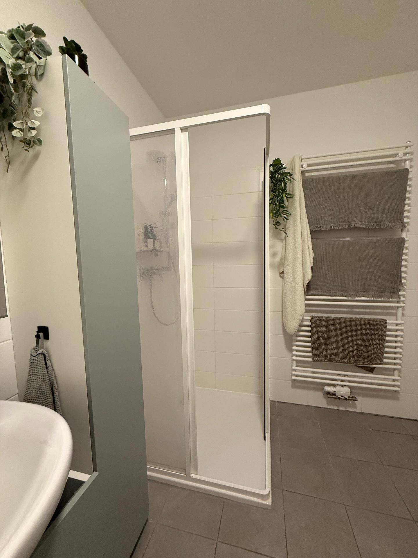 Modernes Badezimmer mit Duschkabine, beheiztem Handtuchhalter und hellen Fliesen.