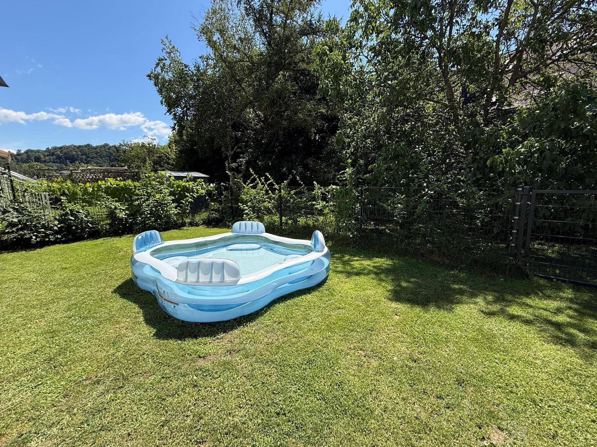 Weitläufiger Gartenbereich mit einem aufblasbaren Pool auf dem Rasen unter blauem Himmel.