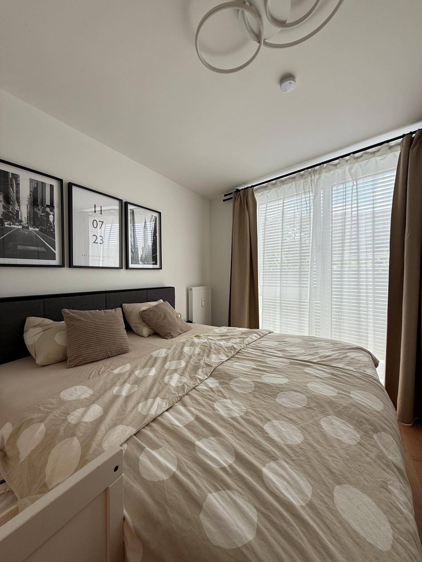 Helles Schlafzimmer mit Doppelbett, Vorhängen und gerahmten Bildern an der Wand.