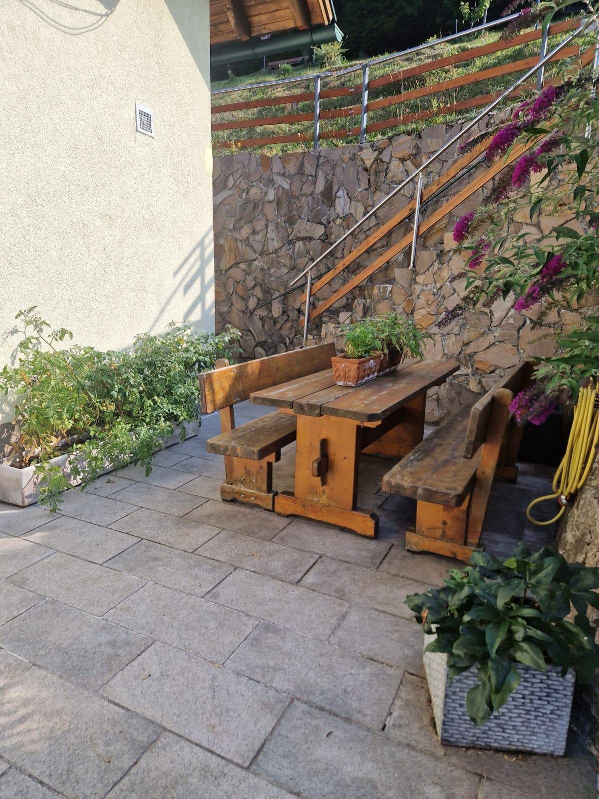 Gepflasterte Terrasse mit rustikalem Holztisch und Bänken, angrenzend an eine Steinmauer.