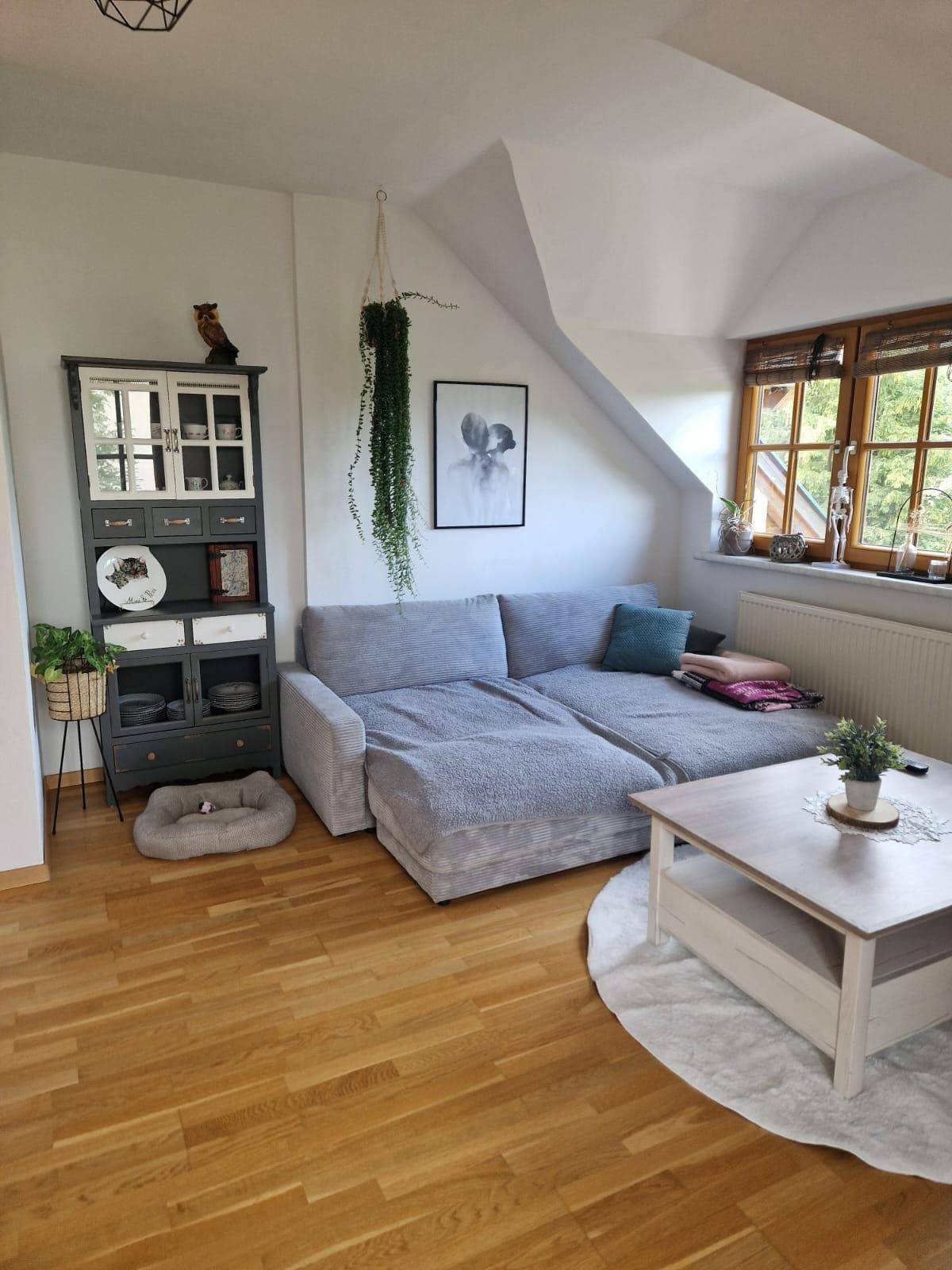 Heller Wohnbereich im Dachgeschoss mit großem Sofa, Schrank und Holzboden.