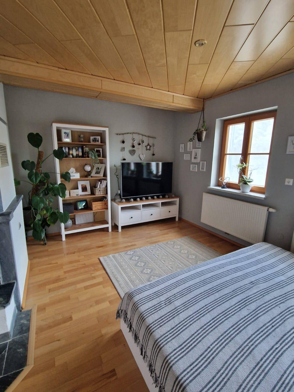 Heller Wohnbereich mit Holzboden, Bücherregal und einem Fenster, das viel Licht hereinlässt.