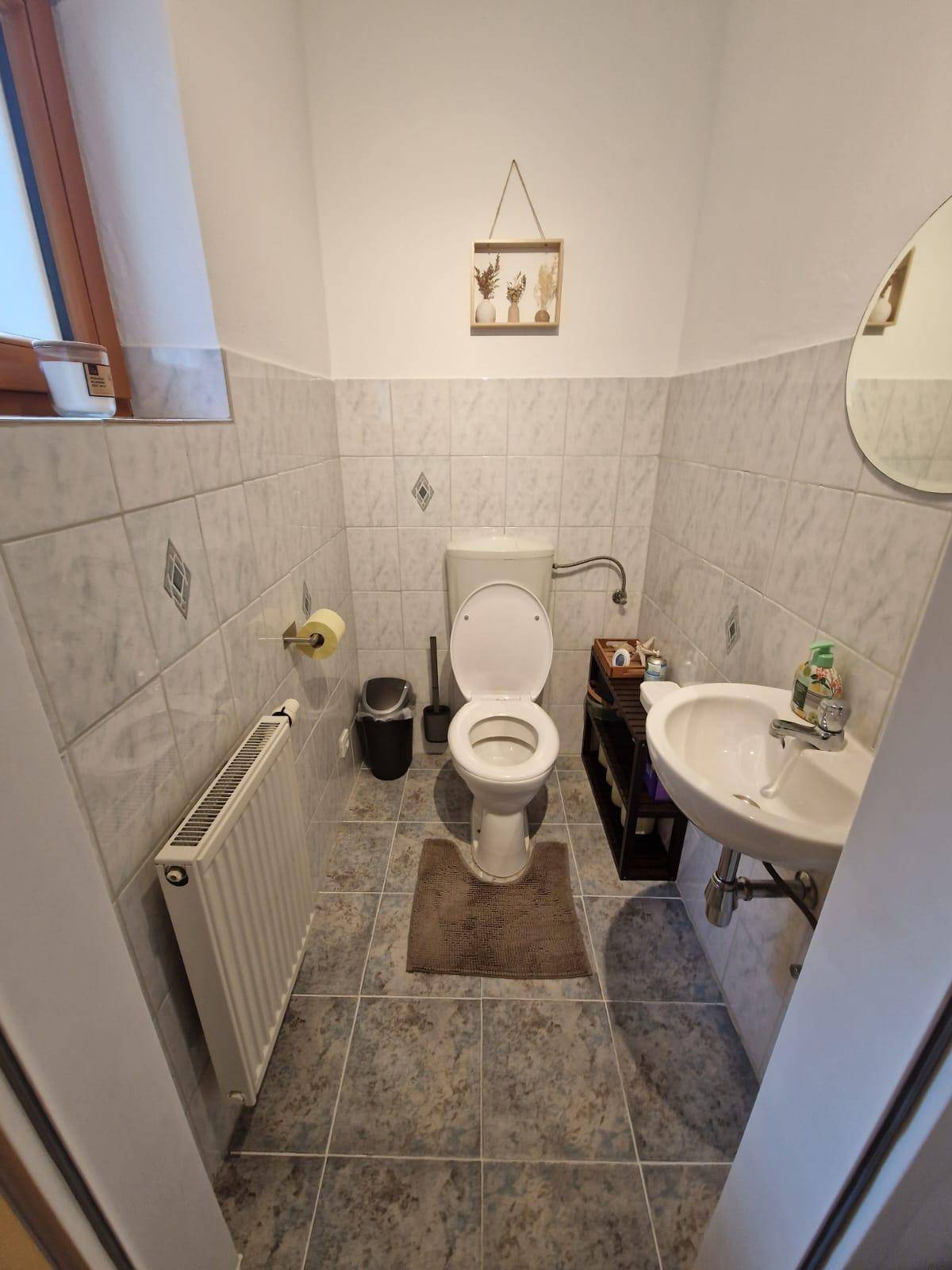 Kleines Gäste-WC mit Toilette, Waschbecken und Fenster, hell gefliest.
