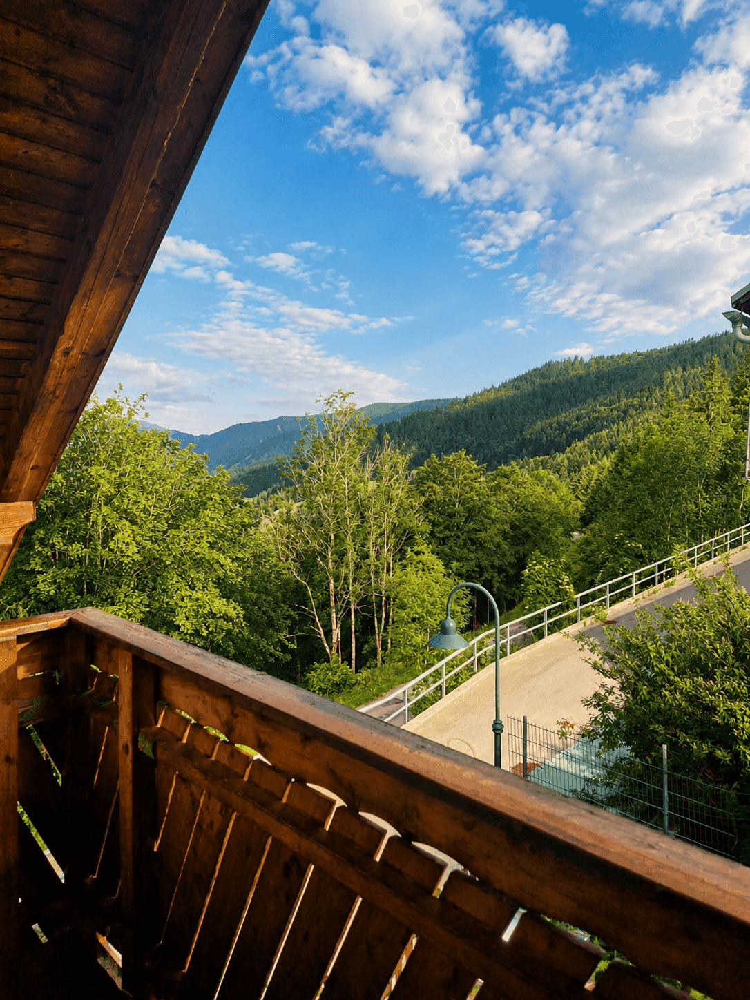 Holzbalkon mit malerischem Blick auf bewaldete Berge und eine darunterliegende Straße.