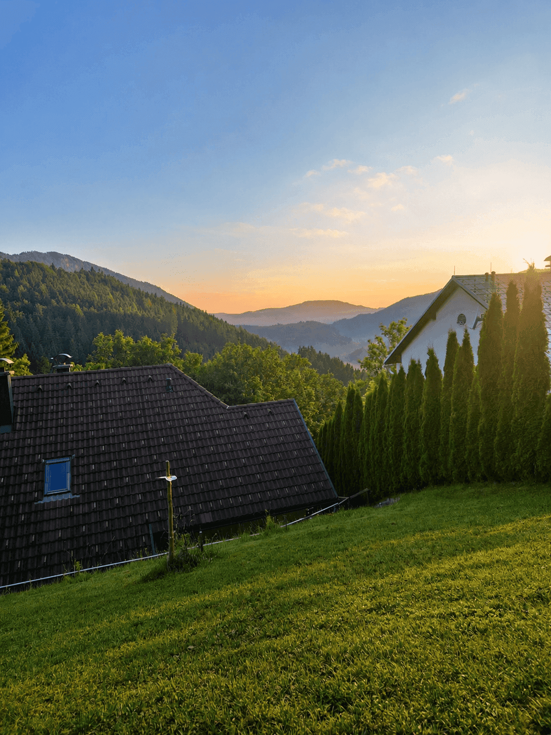 Malerischer Sonnenuntergang über den Bergen mit Blick auf Häuser und grüne Hecken.