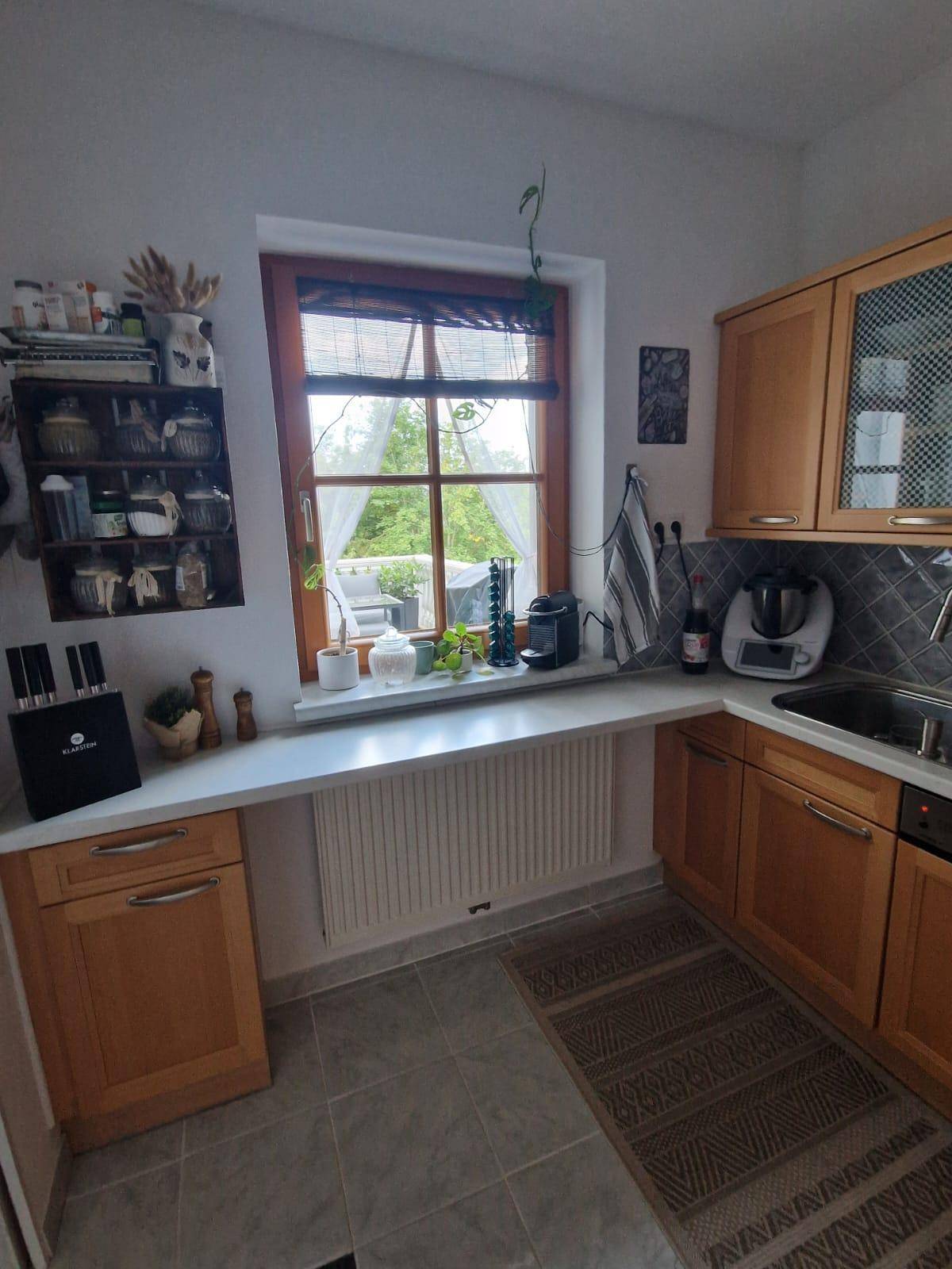 Helle Küche mit Holzschränken, Arbeitsplatte und einem Fenster mit Blick nach draußen.