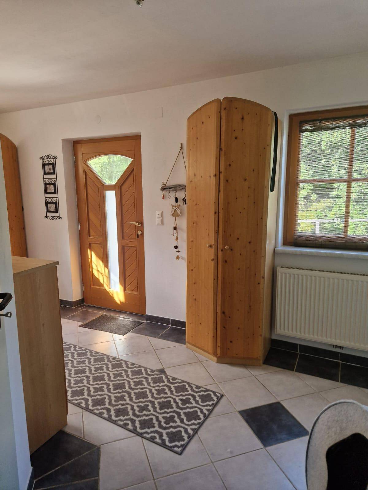 Heller Eingangsbereich mit Fliesenboden, Holzschrank und einer Holztür mit Glaseinsatz.