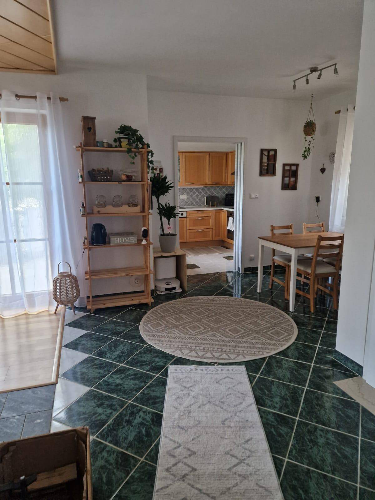 Essbereich mit grünem Fliesenboden und Zugang zu einer Küche mit Holzschränken.