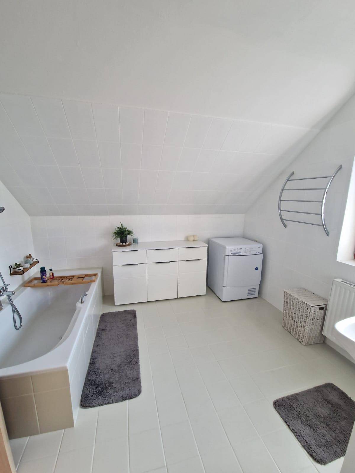 Helles Badezimmer im Dachgeschoss mit Badewanne, Waschmaschine und Dachschräge.