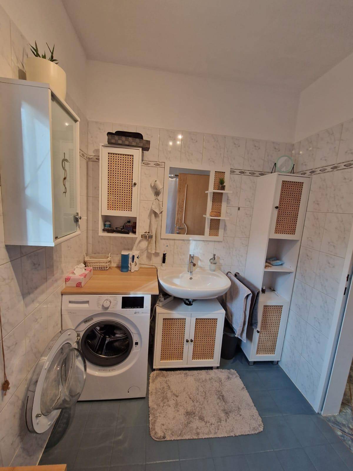 Badezimmer mit Waschmaschine, Waschbecken und Spiegelschrank, hell gefliest.