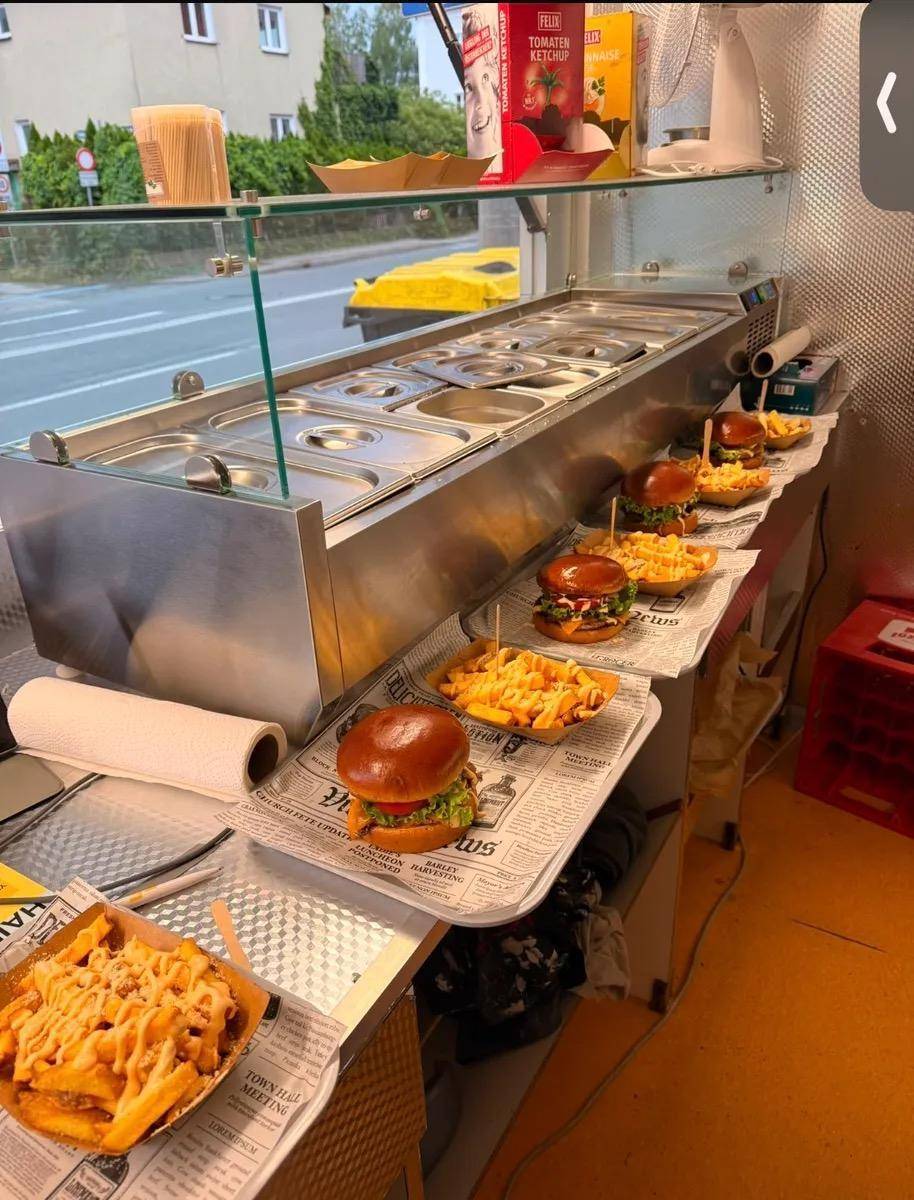 Innenansicht eines Imbisswagens mit zubereiteten Burgern und Pommes Frites auf der Theke und Edelstahlausrüstung.