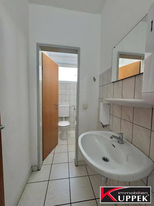 Saubere Gästetoilette mit Waschbecken, Spiegel und weißen Fliesen an Wänden und Boden.