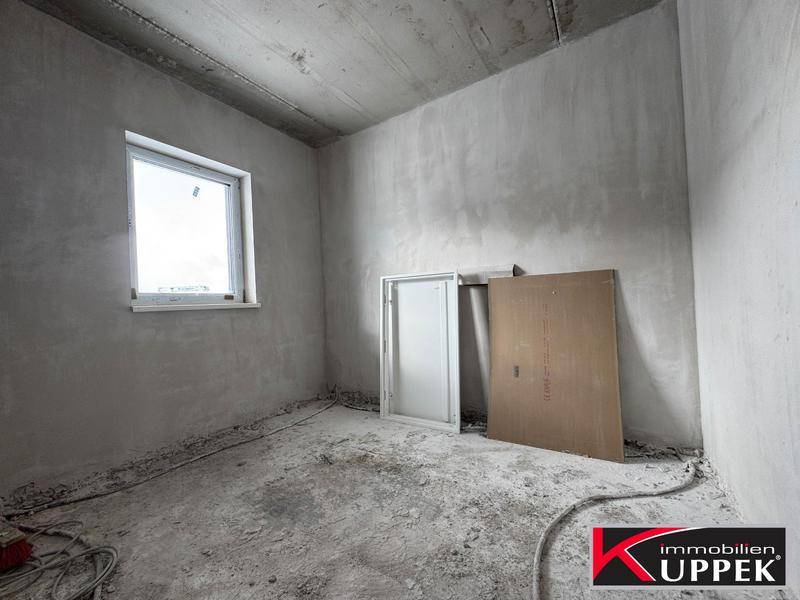 Unfertiges Schlafzimmer im Rohbauzustand mit einem Fenster und Betonwänden.