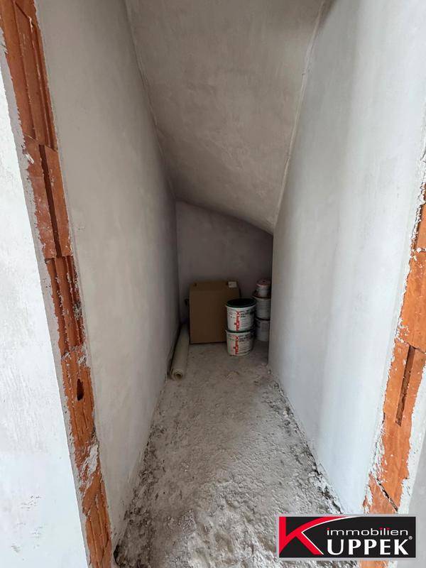 Schmaler Abstellraum im Rohbau mit schrägen Wänden und Betonboden.