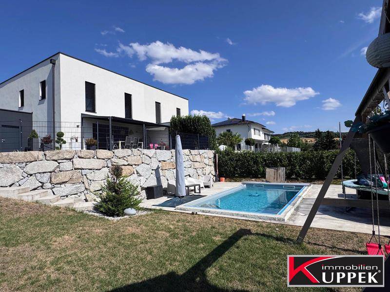 Großzügiger Gartenbereich mit Pool, Schaukel und moderner Hausfassade unter blauem Himmel.