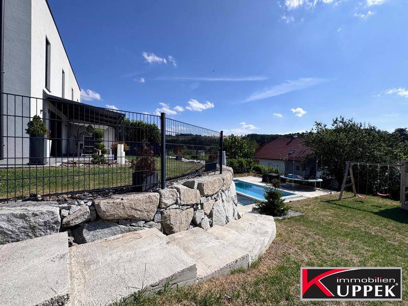 Blick auf den Garten mit Pool, Spielplatz und der modernen Hausfassade im Hintergrund.