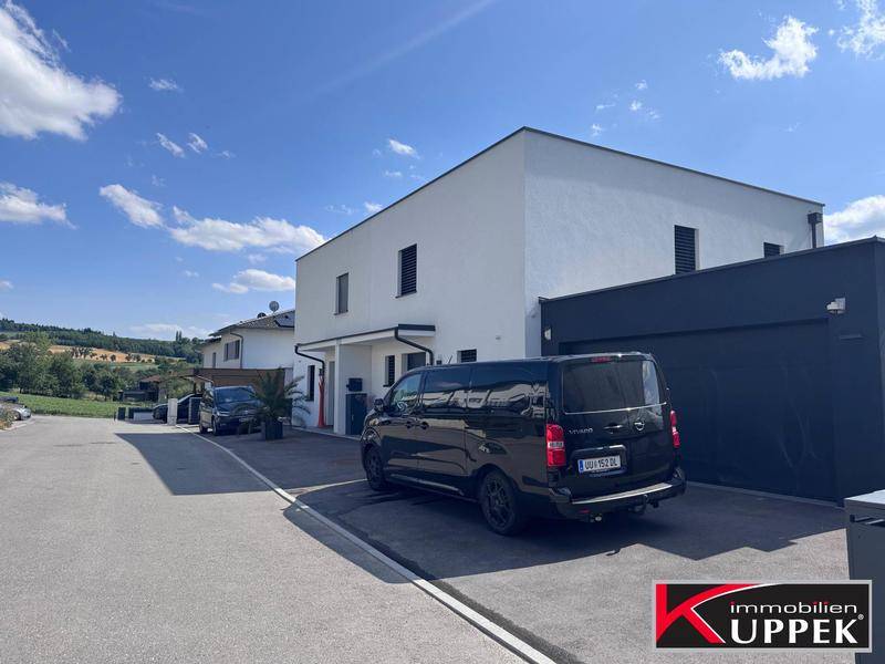 Ansicht der modernen Hausfassade mit Garage und Parkplatz in sonniger Umgebung.