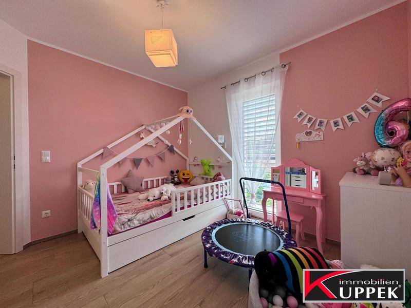 Freundliches Kinderzimmer mit rosa Wänden, Kinderbett und kleinem Trampolin.