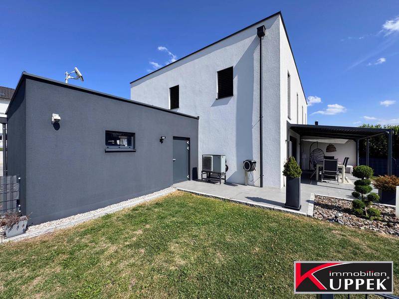 Rückansicht des modernen Hauses mit Garten, Terrasse und Wärmepumpe.
