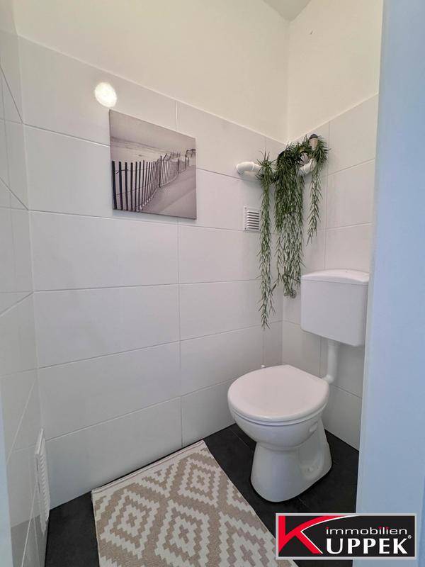Modern gefliestes WC mit Toilette und dekorativer Pflanze, schlicht und funktional.