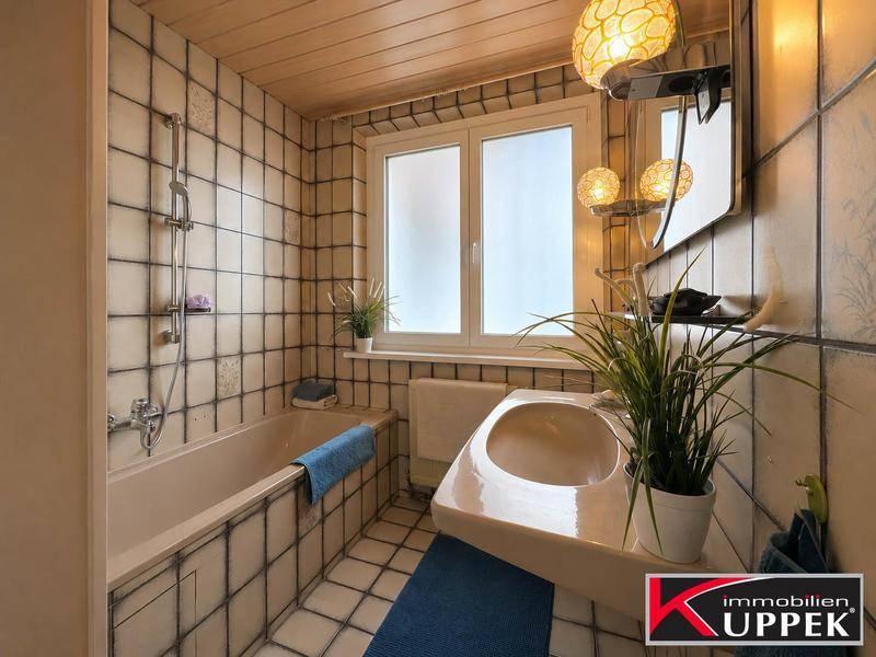Badezimmer mit Badewanne, Waschbecken und hellen Fliesen, ausgestattet mit einem Fenster.