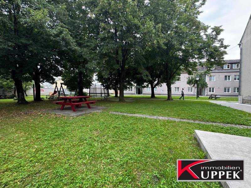 Grüner Gemeinschaftsgarten mit Spielplatz und Picknicktisch, umgeben von Bäumen.