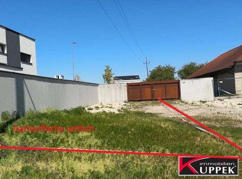 Grasbewachsenes Grundstück mit Schotter, begrenzt durch eine Mauer und angrenzend an moderne Architektur.