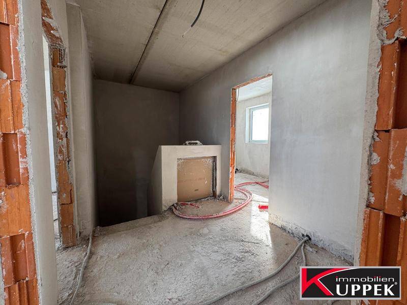 Rohbauflur mit sichtbaren Ziegelwänden und Betonboden, der zu weiteren Räumen führt.