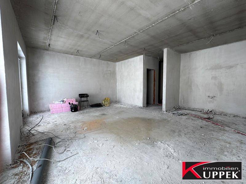 Unfertiger Innenraum im Rohbau mit Betonboden und sichtbaren Installationen, bereit für den Ausbau.