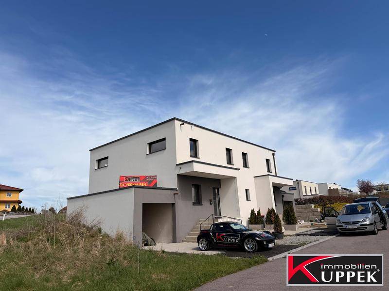 Neubau eines modernen Hauses mit klaren Linien und großzügiger Einfahrt unter blauem Himmel.