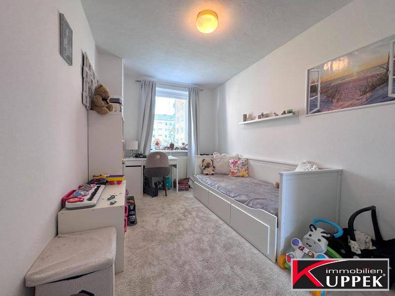 Helles Kinderzimmer mit Teppichboden, Schreibtisch und Spielzeug, ideal zum Lernen und Spielen.