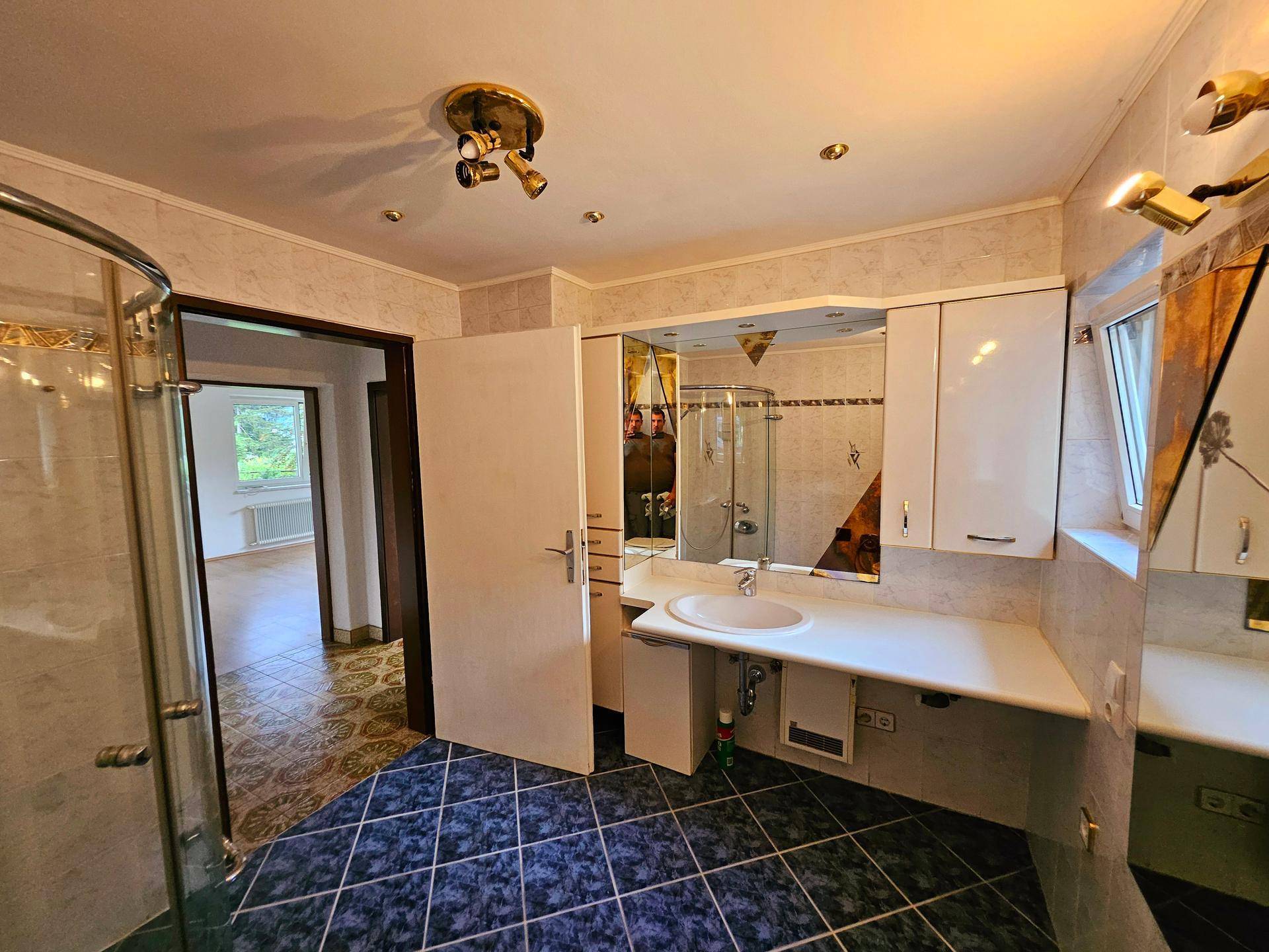Geräumiges Badezimmer mit Dusche, Einzelwaschbecken und dunklen Bodenfliesen.
