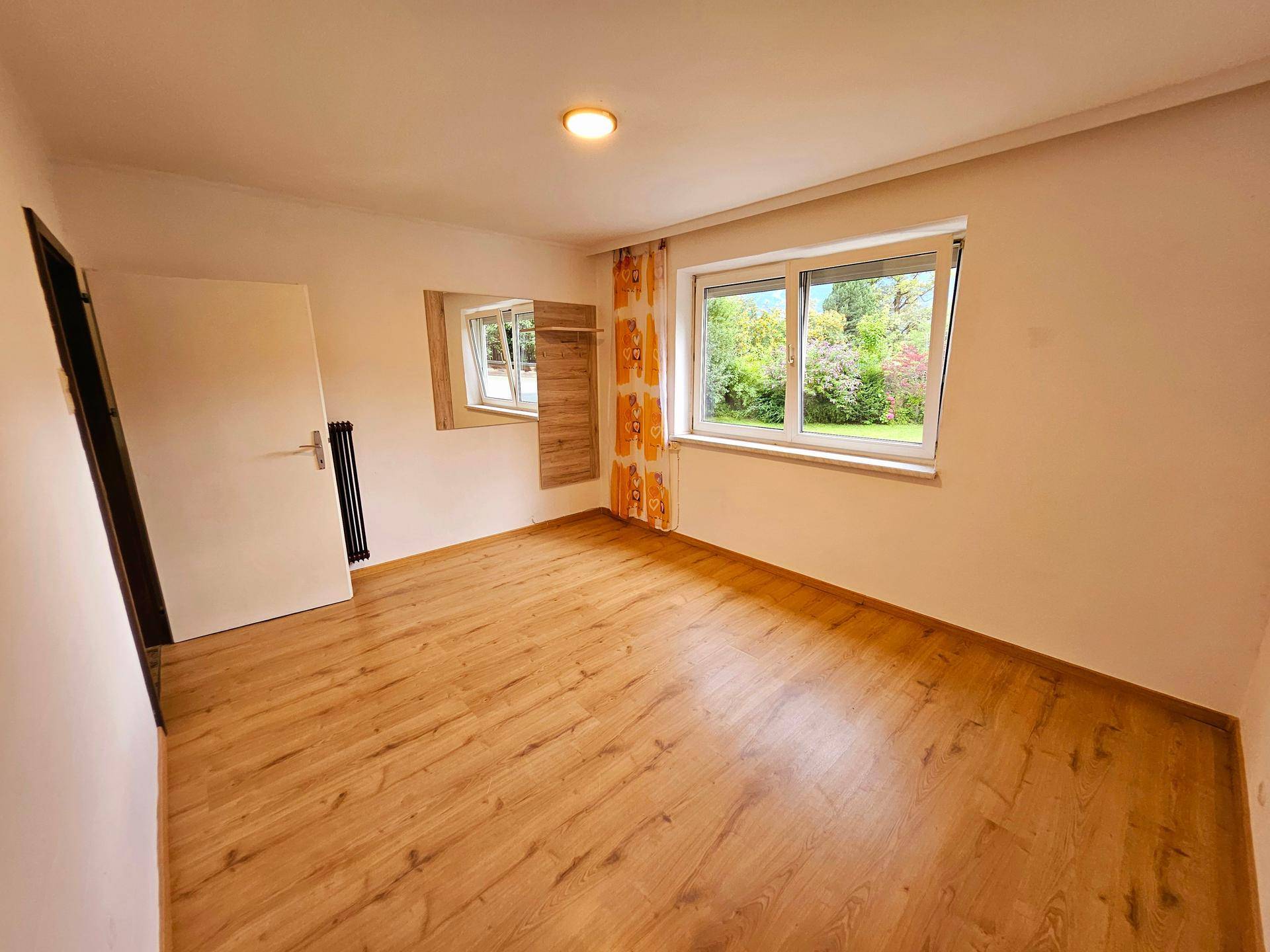 Gemütliches Schlafzimmer mit Laminatboden und einem Fenster, das den Blick ins Grüne freigibt.