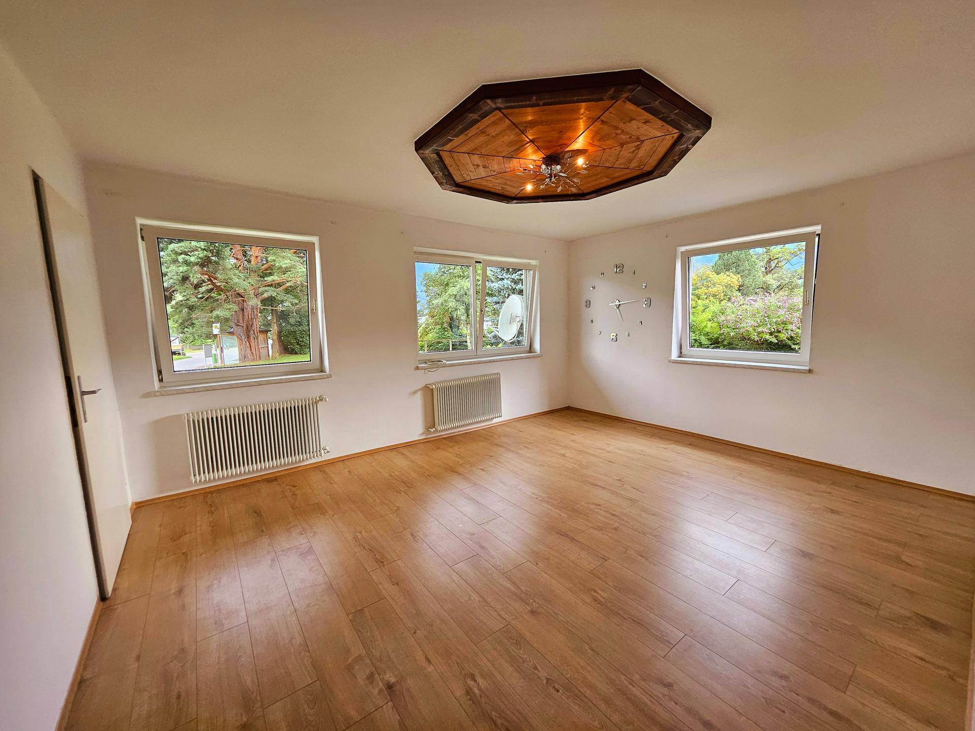 Heller Wohnraum mit Laminatboden, großen Fenstern und einer dekorativen Deckenleuchte.