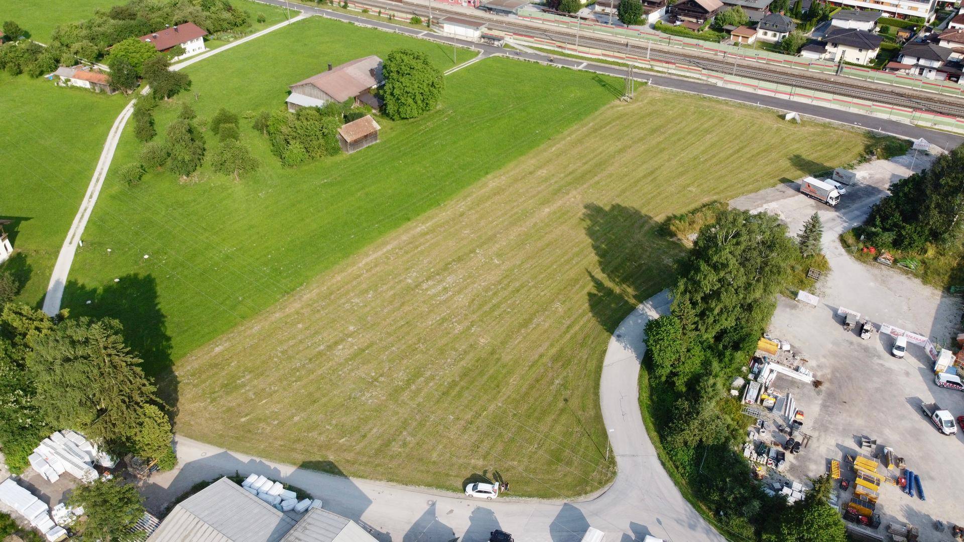 Luftaufnahme eines weitläufigen grünen Feldes mit angrenzenden Gebäuden und einer Straße in ländlicher Umgebung.