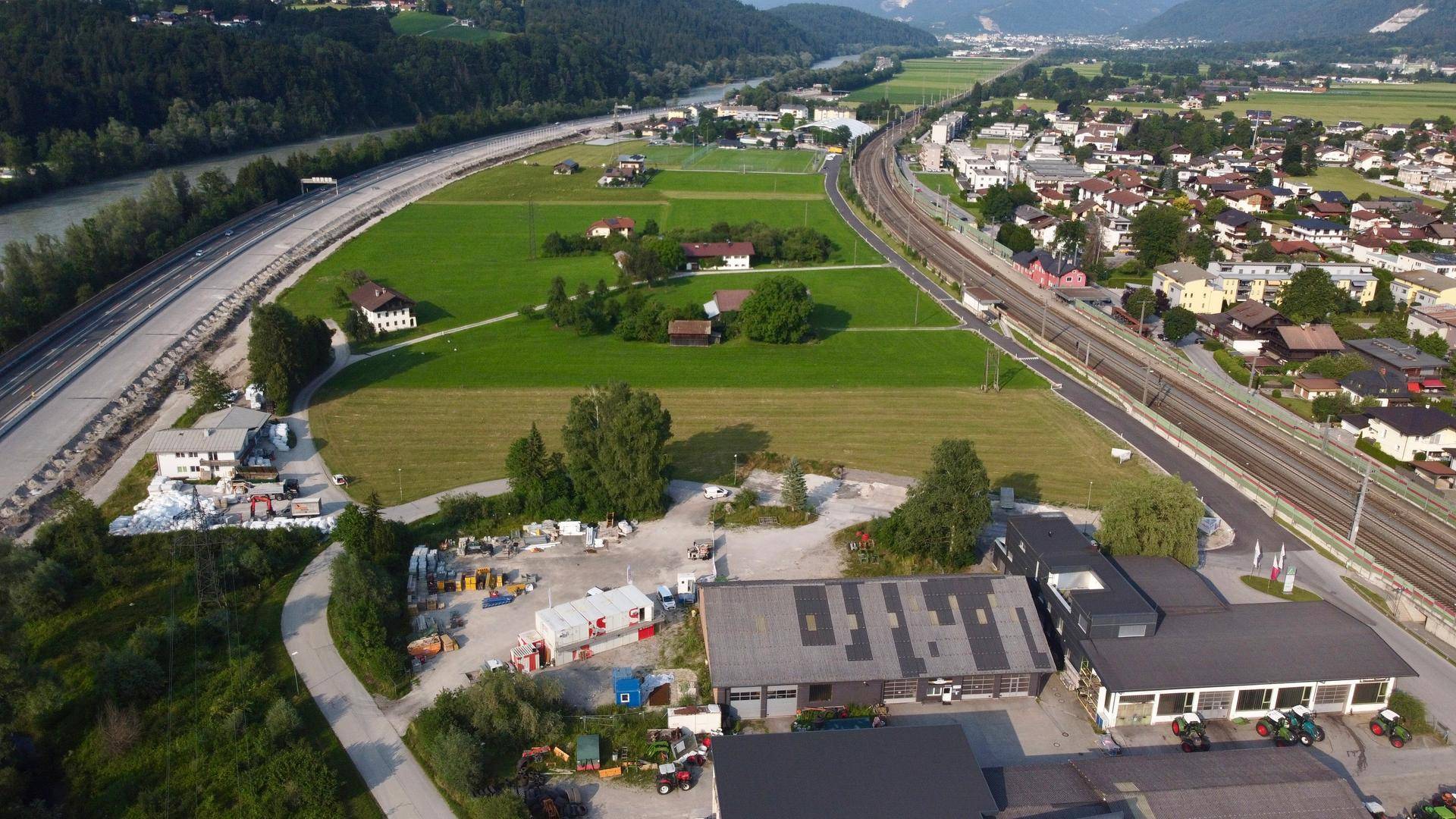 Weitläufige Luftaufnahme einer Flusslandschaft mit Bahngleisen, Feldern und einer kleinen Ortschaft.