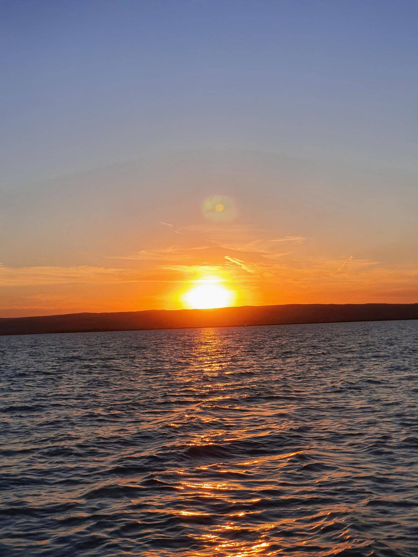 Lebhafter Sonnenuntergang über einem großen Gewässer, der den Himmel widerspiegelt.
