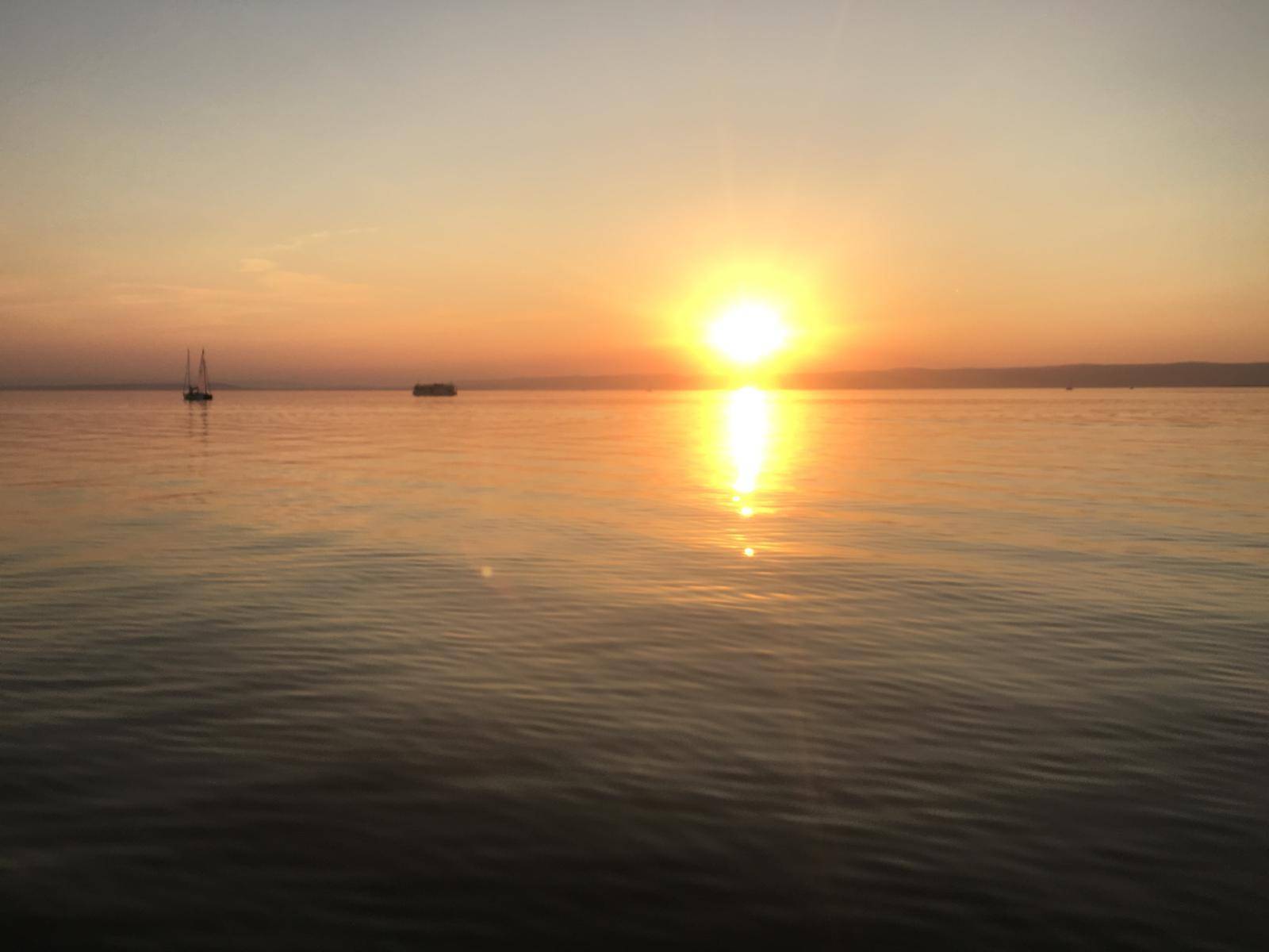 Atemberaubender Sonnenuntergang, der sich auf der ruhigen Seeoberfläche spiegelt, mit einem entfernten Boot.